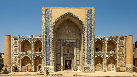 The tiled entrance portal and two-storey facade of Ulugh Beg Madrasa in Bukhara.