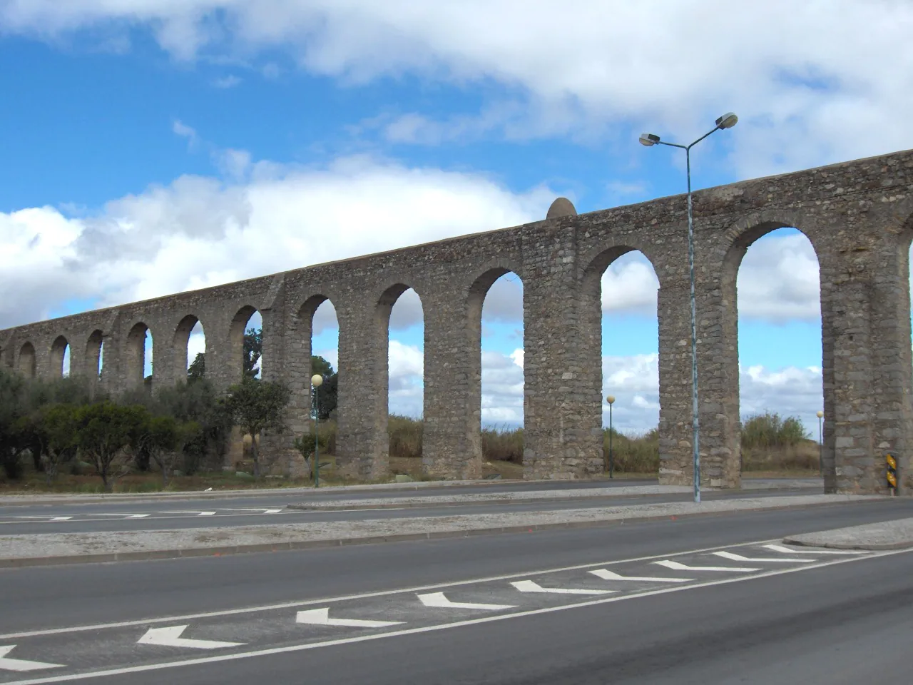 A long row of stone arches carrying the Água de Prata Aqueduct beside a road in Évora.