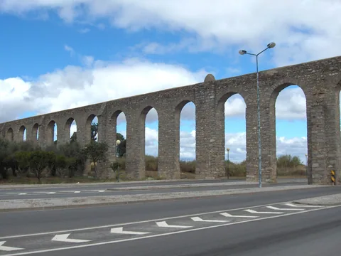 A long row of stone arches carrying the Água de Prata Aqueduct beside a road in Évora.