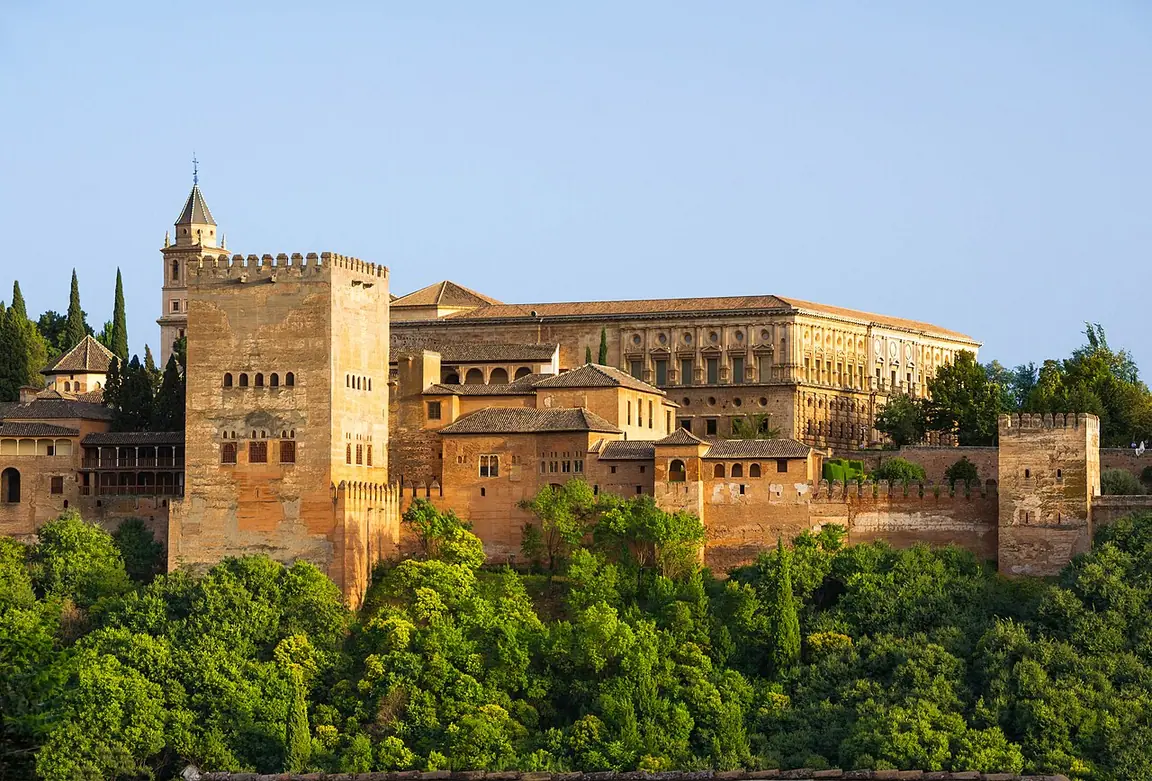 The Comares Tower and Palace of Charles V rise above the walls and wooded hillside of the Alhambra in Granada.