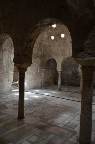 Horseshoe arches, stone columns and small ceiling lights inside El Bañuelo in Granada.