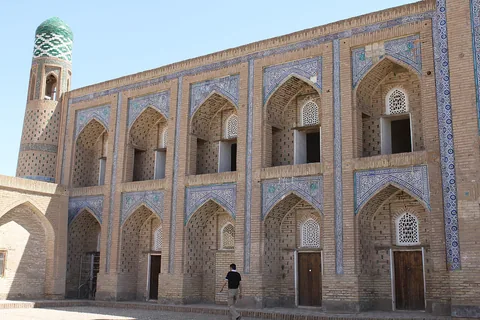 Two levels of pointed arches and blue-white tilework on Muhammad Rahim Khan II Madrasa, beside a green-tiled corner dome.