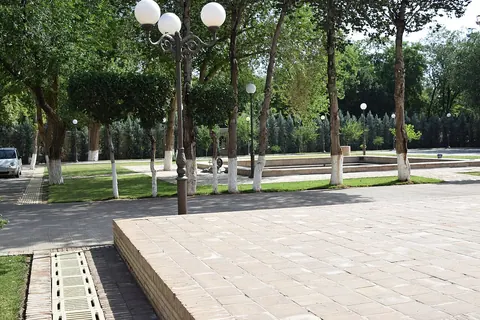 Trees, lawns and paved paths in the grounds of Nurullabay Palace, with garden lamps beside a plain rectangular basin.