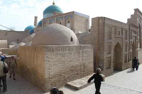 The turquoise dome and tiled upper façade of Pahlavan Mahmud Mausoleum rise above brick tombs beside a narrow lane.