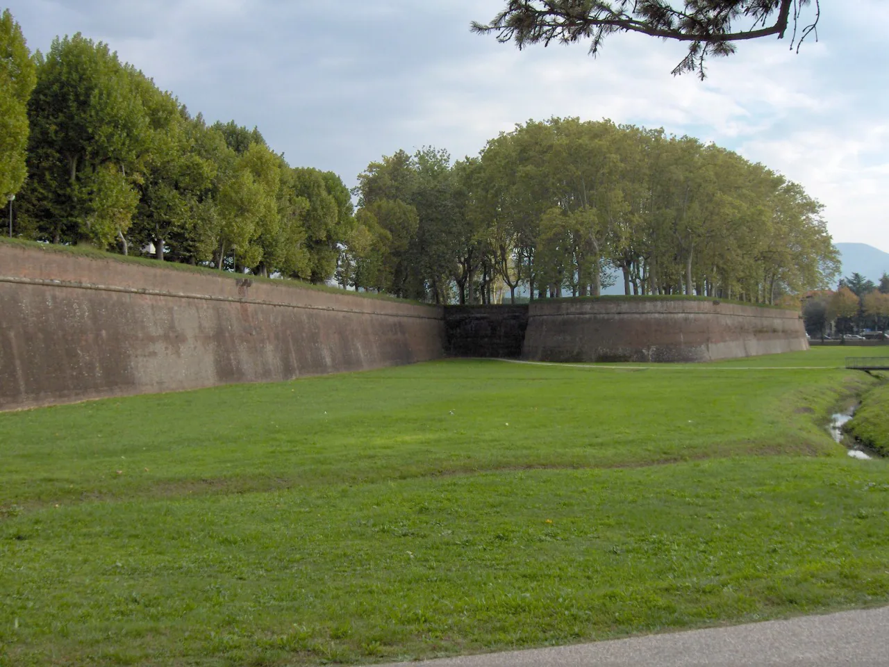 Brick outer face of Lucca's city walls with a grassy foreground and trees on the broad rampart
