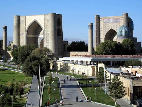 The monumental portals and turquoise dome of Bibi-Khanym Mosque behind a tree-lined pedestrian approach.