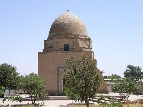 The plain brick Rukhobod Mausoleum has a rounded dome above an octagonal drum, with trees in front.