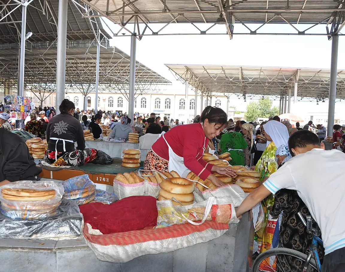 Vendors and customers handle stacks of round Samarkand bread under the covered roof of Siyob Bazaar.