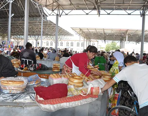 Vendors and customers handle stacks of round Samarkand bread under the covered roof of Siyob Bazaar.