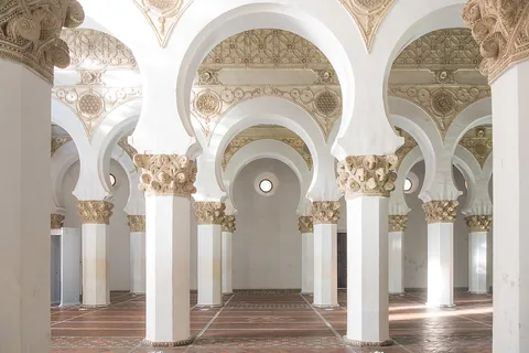 White octagonal pillars, carved capitals and horseshoe arches inside Santa María la Blanca in Toledo.
